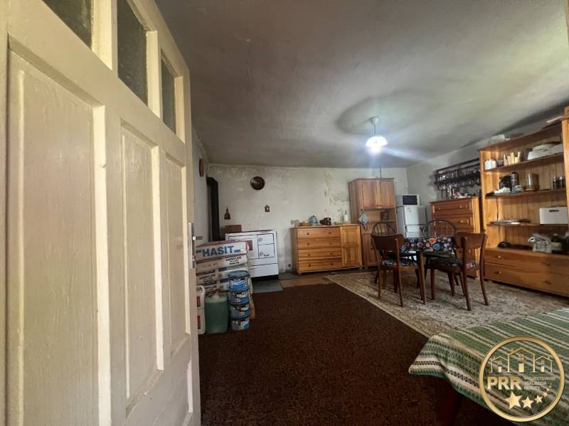 !! NOVÁ CENA !! predaj romantickej chalúpky v Šípkove  - Interiér s dreveným nábytkom, kobercom, stolom a chata dodáva rustikálnu atmosféru.