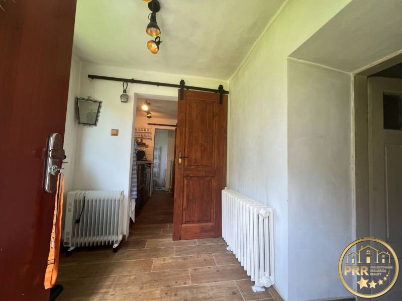 !! NOVÁ CENA !! predaj romantickej chalúpky v Šípkove  - Interiér chaty s podlahou s dreveným dekorom, radiátorom a jazdnou drevenou dverou.