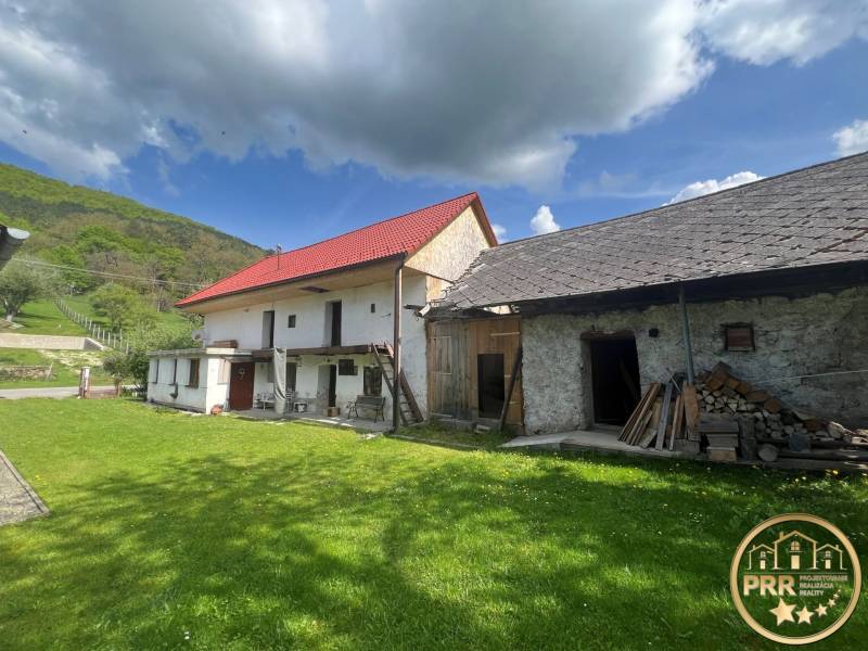 !! NOVÁ CENA !! predaj romantickej chalúpky v Šípkove  - Vidiecke domy s červenou strechou, kamenitý exteriér, zelený trávnik, les a modrá obloha.