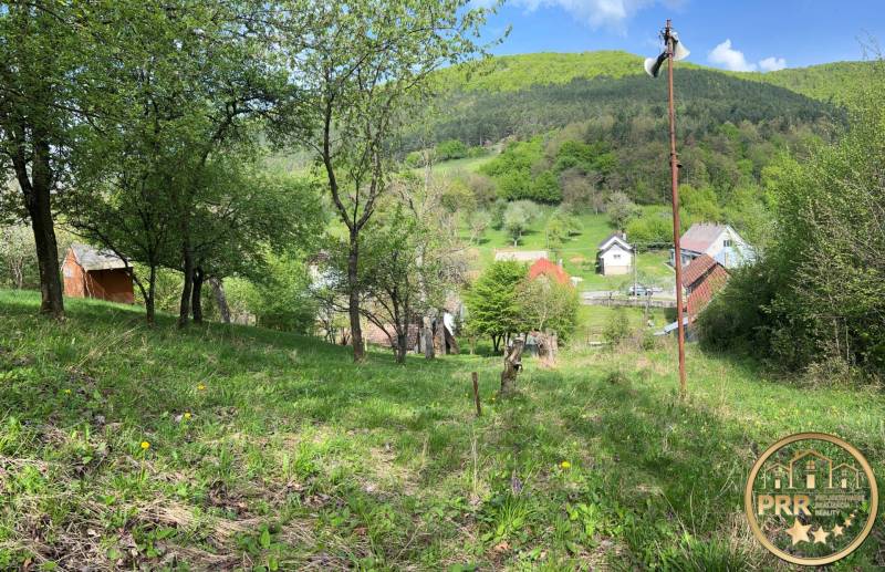 !! NOVÁ CENA !! predaj romantickej chalúpky v Šípkove  - Krásna prírodná scenéria s chatou, stromami a malebnou dedinkou na pozadí kotliny.