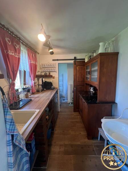 !! NOVÁ CENA !! predaj romantickej chalúpky v Šípkove  - Kuchyňa v drevenej chate s rustikálnym nábytkom, umývadlom a dekoratívnymi záclonami.