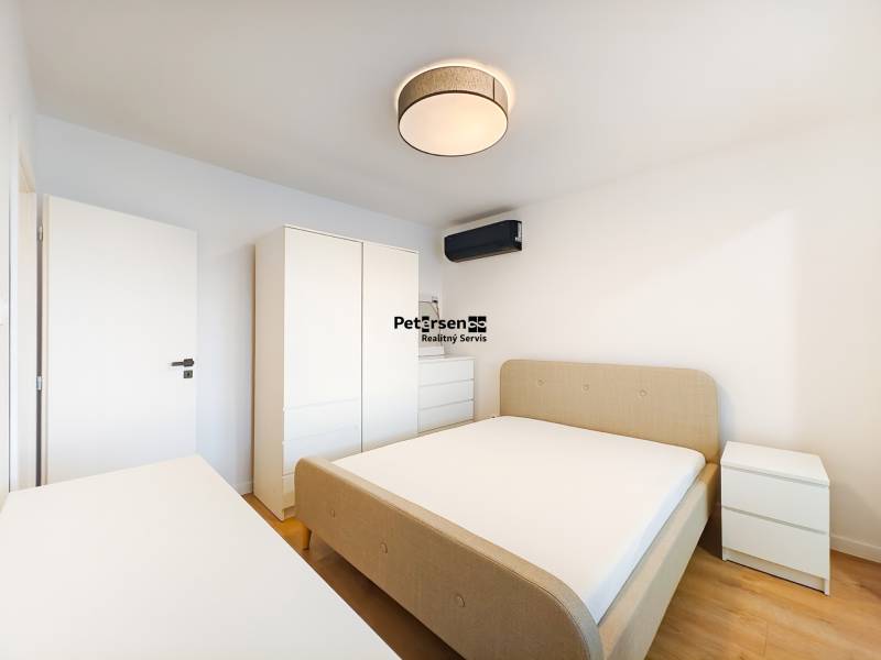 Prenájom úplne nového 2 izb. bytu - skvelá poloha a komfortné bývanie. - Spálňa v 2-izbovom byte s posteľou, skriňou, komodou a podlahou s dreveným dekorom.