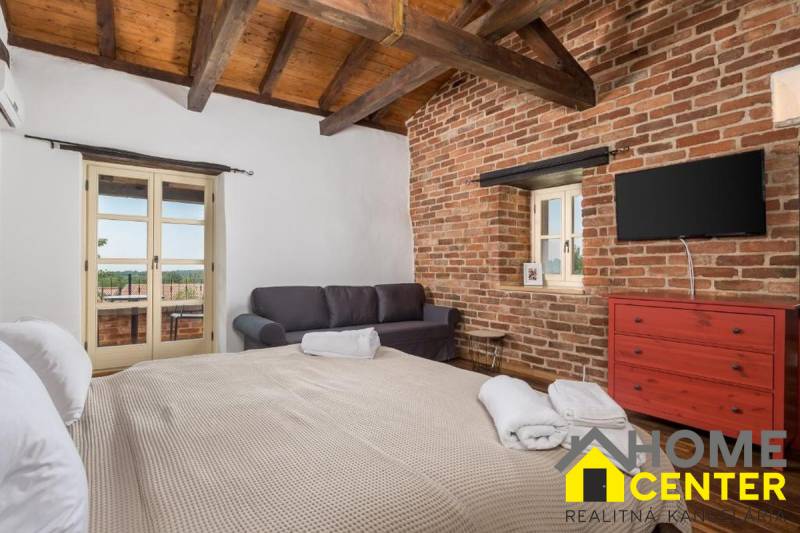 Na predaj KAMENNÝ DOM s LUXUSOM v srdci Istrie - Spálňa vo vile s tehlovými stenami, TV, pohovkou a veľkou posteľou.