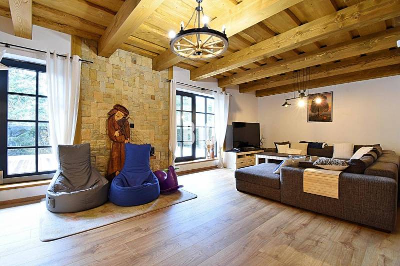 LUKRATÍVNA CHATA - NOVOSTAVBA - SRDCE VRÁTNEJ DOLINY - Interiér Chaty s kamennou stenou, veľkým gaučom a podlahou s dreveným dekorom.