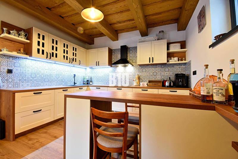 LUKRATÍVNA CHATA - NOVOSTAVBA - SRDCE VRÁTNEJ DOLINY - Kuchyňa v chate s dreveným stropom, podlahou s dreveným dekorom a modrými obkladmi.