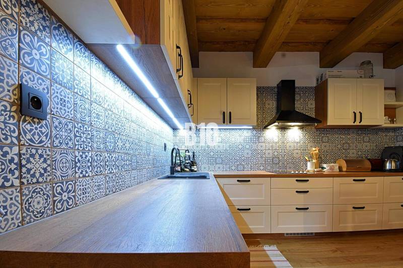 LUKRATÍVNA CHATA - NOVOSTAVBA - SRDCE VRÁTNEJ DOLINY - Kuchyňa v chate s dlaždicami a podlahou s dreveným dekorom, osvetlená LED svetlami.