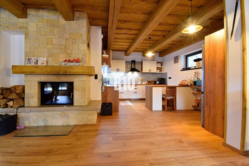 LUKRATÍVNA CHATA - NOVOSTAVBA - SRDCE VRÁTNEJ DOLINY - Interiér chaty s kachľovým krbom, dreveným stropom a podlahou s dreveným dekorom.