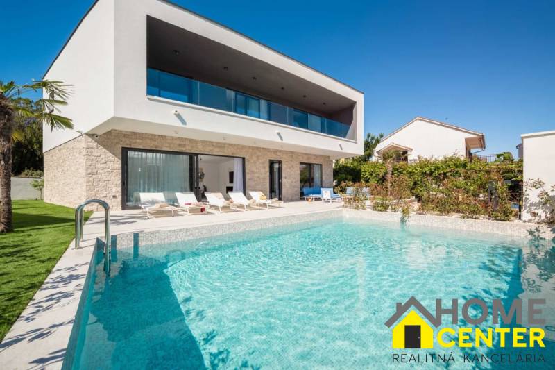 NA PREDAJ novo postavená VILA  /200 m2/ pri mori, Rogoznica - Vila v Bale s bazénom a ležadlami, obklopená zeleňou a modrou oblohou.