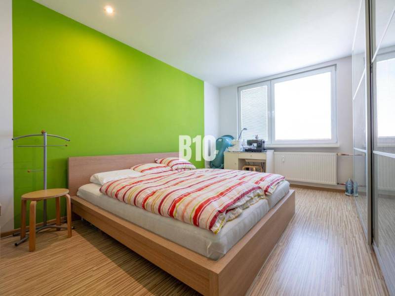 Príjemný 4 izbový byt s balkónom - Klokočina - Spálňa v 4-izbovom byte s podlahou s dreveným dekorom a zelenou stenou.