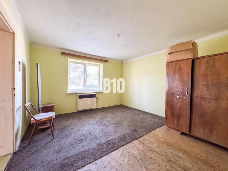 Rodinný dom s veľkým pozemkom (4641 m2)  - Ondrejovce - Jednoduchá izba v rodinnom dome s kobercom a dreveným nábytkom.