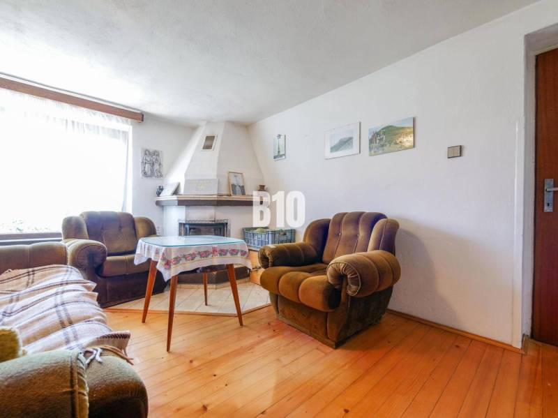 Rodinný dom s nádherným 8 árovým pozemkom na Kamennej ulici - Rodinný dom s krbom, pohodlnými kreslami a podlahou s dreveným dekorom.