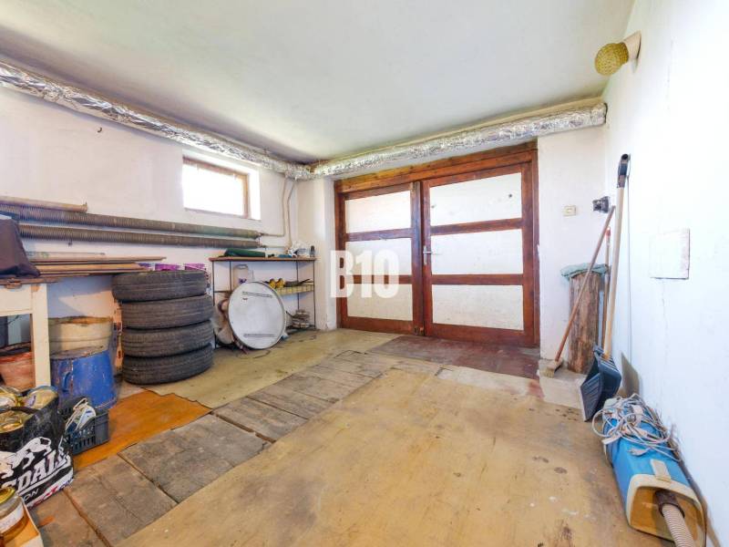 Rodinný dom s nádherným 8 árovým pozemkom na Kamennej ulici - Garáž v rodinnom dome s drevenými dverami a podlahou podobnou drevenému dekoru.