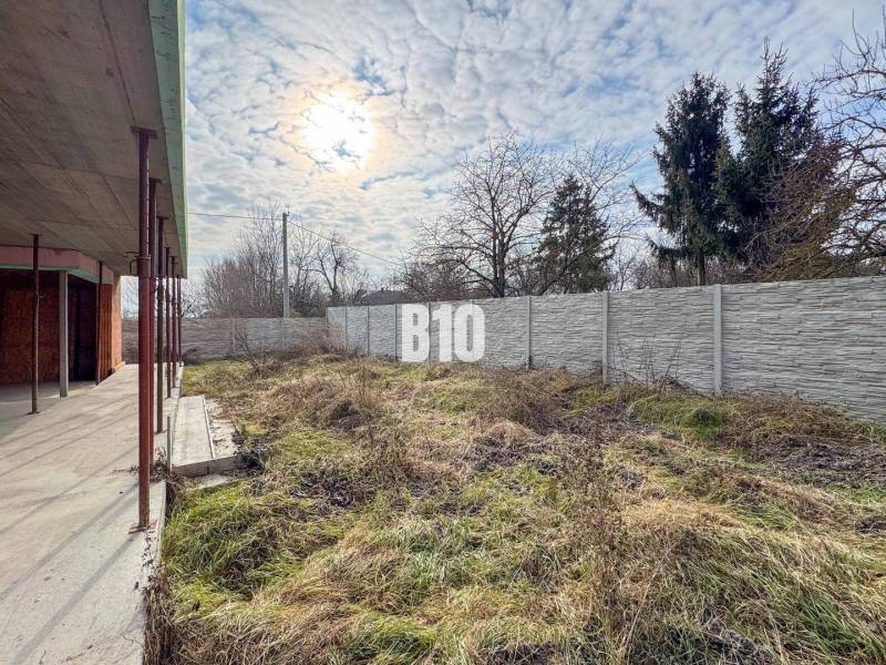 6 izbový rodinný dom  - DVOJGARÁŽ - CABAJ časť Riegler - Stavba rodinného domu s trávnatým pozemkom a oplotením, pod zamračenou oblohou.