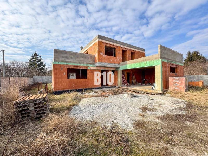 6 izbový rodinný dom  - DVOJGARÁŽ - CABAJ časť Riegler - Nedokončená stavba tehlového rodinného domu, obklopená trávou a drevenými paletami.