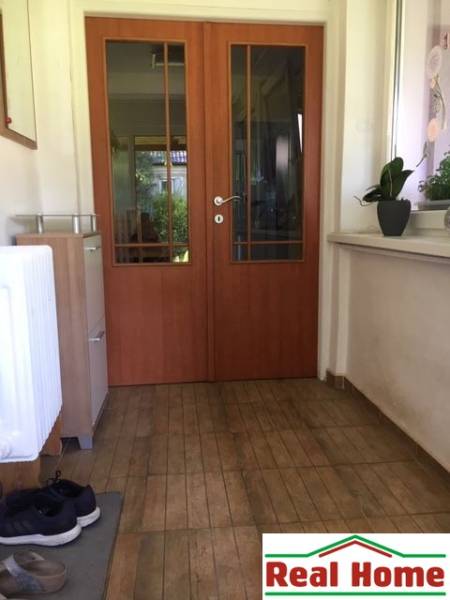 Dom s garážou na peknom rovinatom pozemku so šírkou 24m. - V rodinnom dome: predsieň s dverami, podlaha s dreveným dekorom, rastliny na parapete.