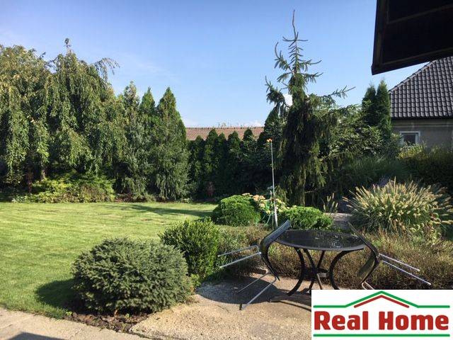 Dom s garážou na peknom rovinatom pozemku so šírkou 24m. - Záhrada rodinného domu v Čiernej Vode s trávnikom, stromami a vonkajším sedením.