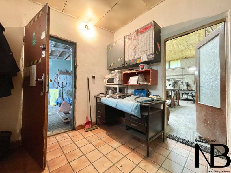 Na predaj objekt vhodný na podnikanie – Trenčín, Záblatie - Interiér obchodných priestorov s dlažbou, pracovným stolom a náradím na poličkách.