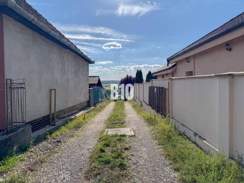 Stavebný pozemok so stavebným povolením - Janíkovce - 729 m2 - Úzka cesta medzi domami v lokalite Pozemky - bývanie, Nitra, vedúca k panoráme krajiny.