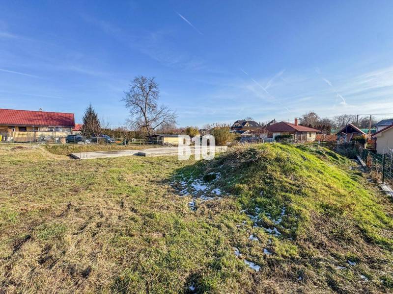 1786 m2 - základová doska - stavebné povolenie + projekt - Mojmírovce - Pozemok pripravený na stavbu bývania, zasnežená tráva, obklopený domami a strešnými krytinami.