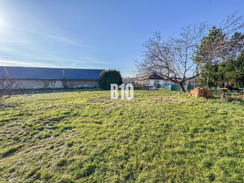 1786 m2 - základová doska - stavebné povolenie + projekt - Mojmírovce - Pozemok s trávnikom, stromom a stavbou na bývanie v pozadí.