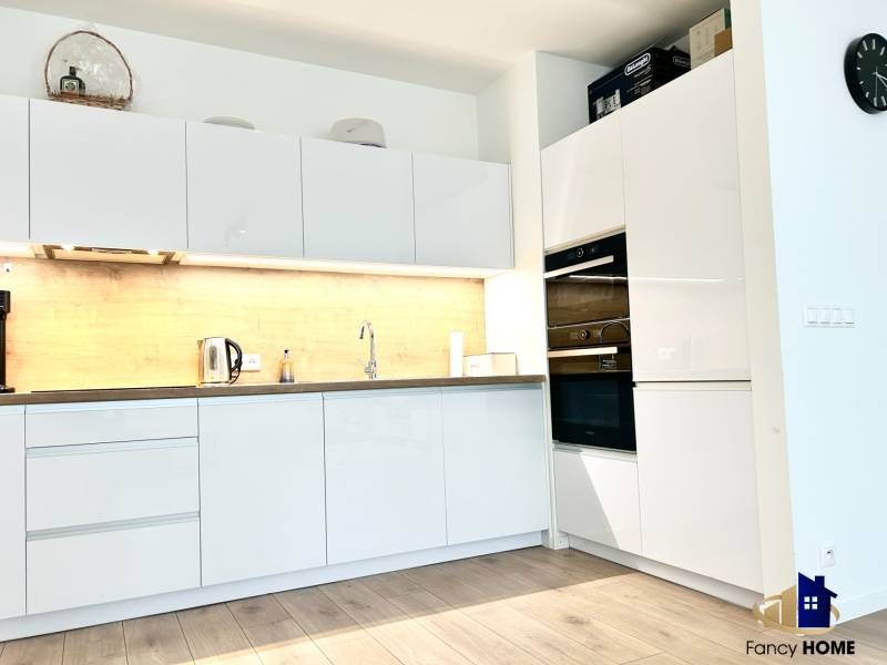 PRENÁJOM exkluzívny 2 izb byt POPRAD s loggiou 53,9 + 8,34 m2 - Kuchyňa v 2-izbovom byte s bielymi skrinkami a podlahou s dreveným dekorom.