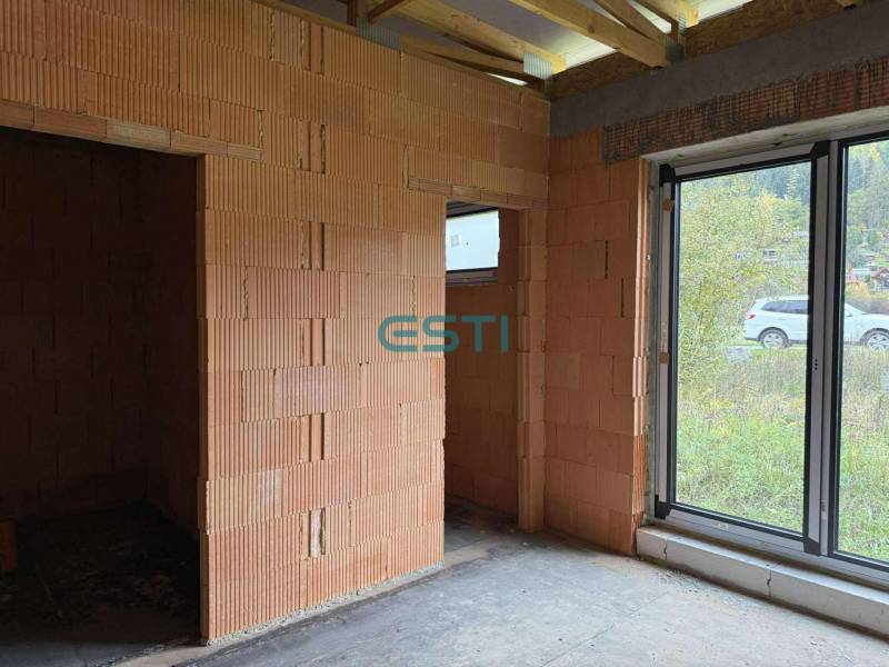 Rodinný dom - bungalov, Teplička nad Váhom - Nedokončený interiér v rodinnom dome s veľkým oknom a tehlovými stenami.