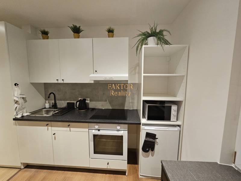 Kompletne zrekonštruovaná garsónka - BA Nové mesto - Kuchyňa v garsónke s bielymi skrinkami a podlahou s dreveným dekorom.