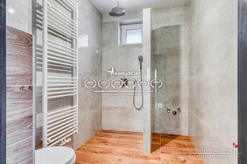 3-izbový moderne zrekonštruovaný rodinný dom v obci Jaslovské Bohunice - Sprchový kút v rodinnom dome s podlahou s dreveným dekorom a svetlými obkladmi.