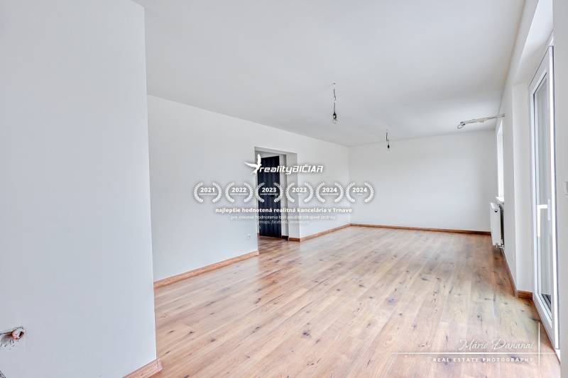 3-izbový moderne zrekonštruovaný rodinný dom v obci Jaslovské Bohunice - Priestranná izba v rodinnom dome s podlahou s dreveným dekorom a bielymi stenami.