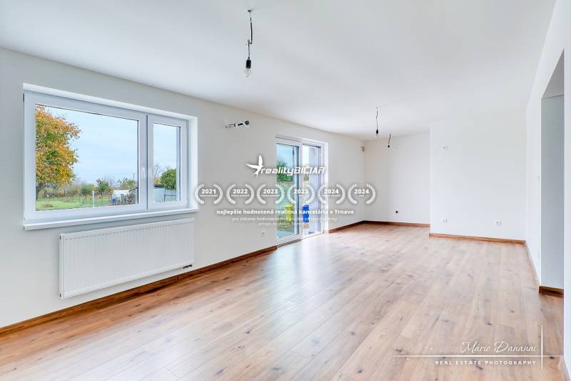 3-izbový moderne zrekonštruovaný rodinný dom v obci Jaslovské Bohunice - Priestranná obývacia izba v Rodinnom dome s podlahou s dreveným dekorom a veľkými oknami.