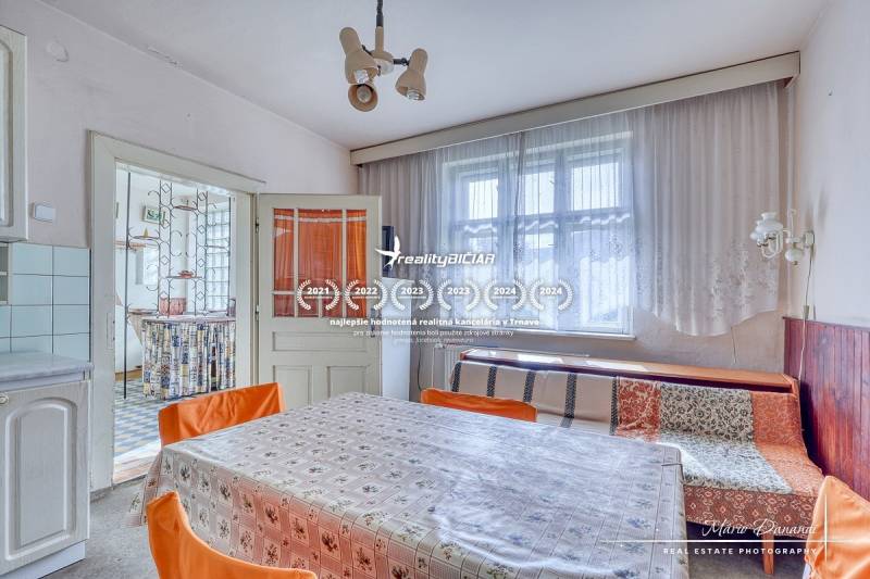 REZERVOVANÉ Starší 2-izbový rodinný dom v obci Dobrá Voda - Jedáleň v rodinnom dome s veľkým oknom, kvetinovým obrusom a oranžovými stoličkami.