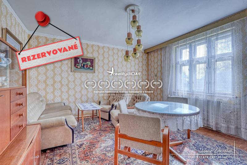 REZERVOVANÉ Starší 2-izbový rodinný dom v obci Dobrá Voda - Interiér rodinného domu s vintage nábytkom, tapetami a veľkým oknom s čipkovanou záclonou.