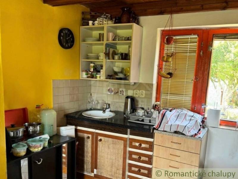 Záhrada s chatkou pod Malými Karpatami, Sološnica - Kuchyňa v chate s dreveným stropom a žltou stenou, vybavená základným riadom.