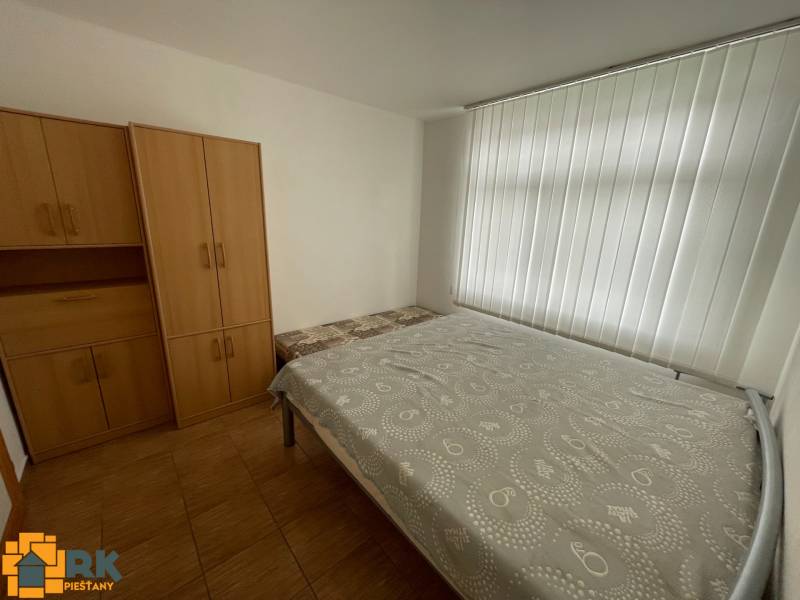 Predaj budovy v centre mesta - Spálňa v rodinnom dome s bielymi roletami, posteľou a skriňami.