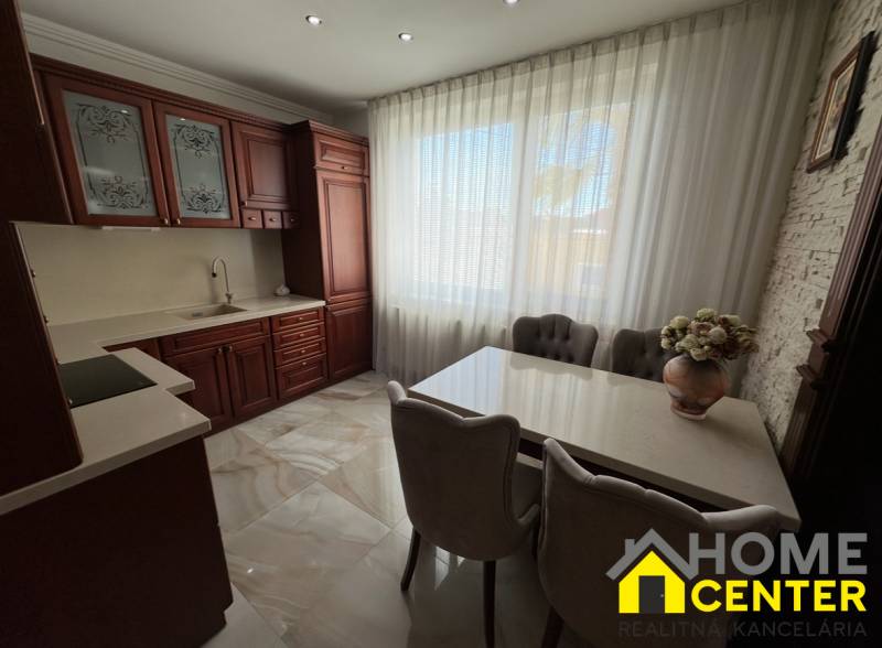 PREDAJ : ŠTÝLOVÝ RODINNÝ DOM S BAZÉNOM, KOMÁRNO - Kuchyňa s tmavými skrinkami, bielymi závesmi a kvetinovou dekoráciou v rodinnom dome.