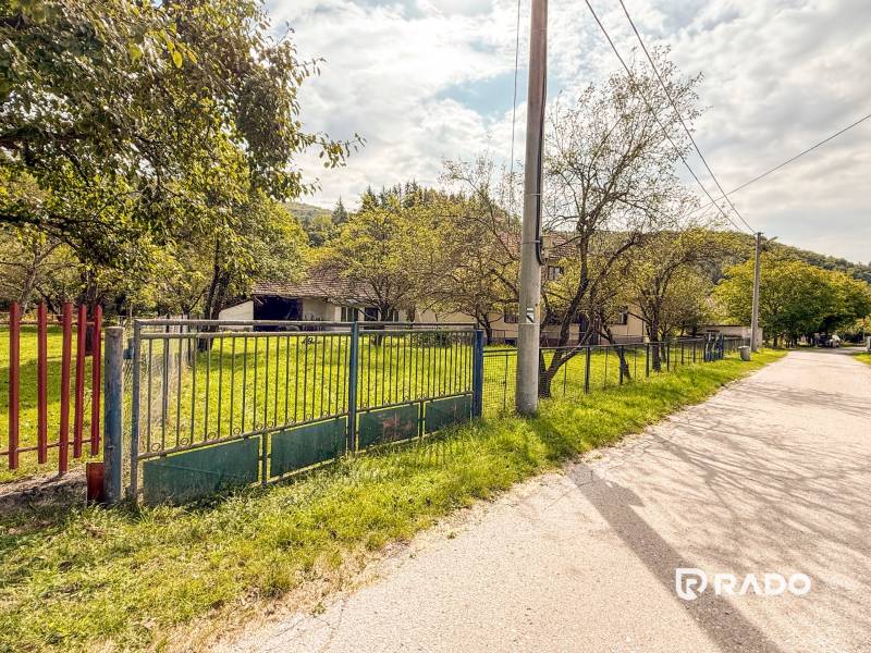 5i RD s garážou, Čierna Lehota, okr. Bánovce n./B. - Rodinný dom v Čiernej Lehote s veľkou záhradou a kovovým plotom pri ceste.