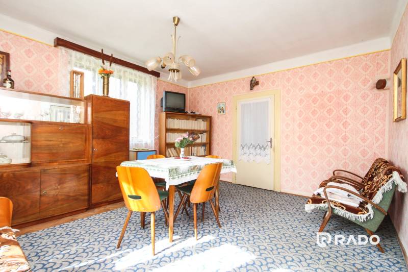 5i RD s garážou, Čierna Lehota, okr. Bánovce n./B. - Interiér rodinného domu s retro nábytkom, kobercom a svetlými stenami s tapetou.