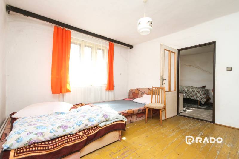 5i RD s garážou, Čierna Lehota, okr. Bánovce n./B. - Izba s posteľou a kreslom, podlaha s dreveným dekorom, oranžové závesy, rodinný dom.