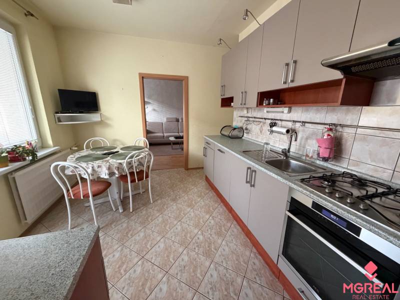 3 izbový byt  balkónom Topoľčany Juh - Kuchyňa v 3-izbovom byte s rohovou linkou, stolom a televízorom na stene.