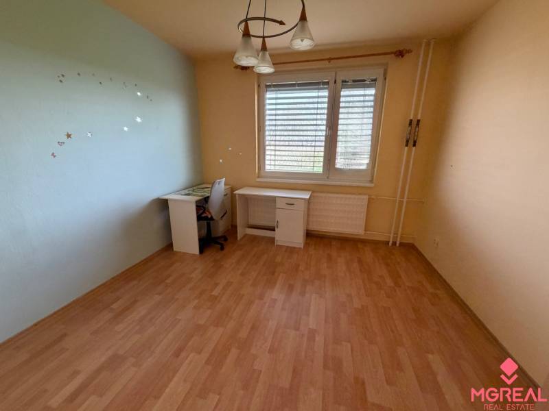 3 izbový byt  balkónom Topoľčany Juh - Izba v 3-izbovom byte s podlahou s dreveným dekorom a pracovným stolom.