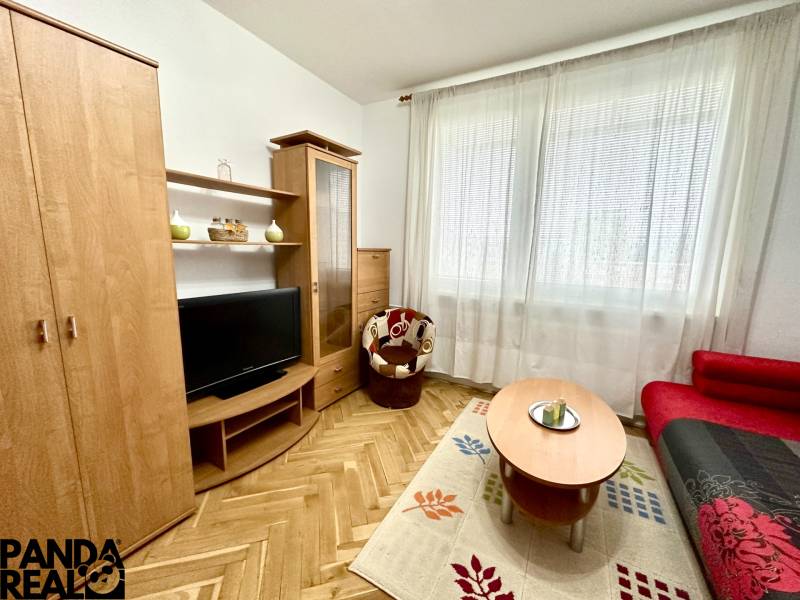 GARSONKA NA PRENÁJOM – VOĽNÁ IHNEĎ (sídlisko Východ) - Garsónka s televízorom, červeným gaučom a podlahou s dreveným dekorom.