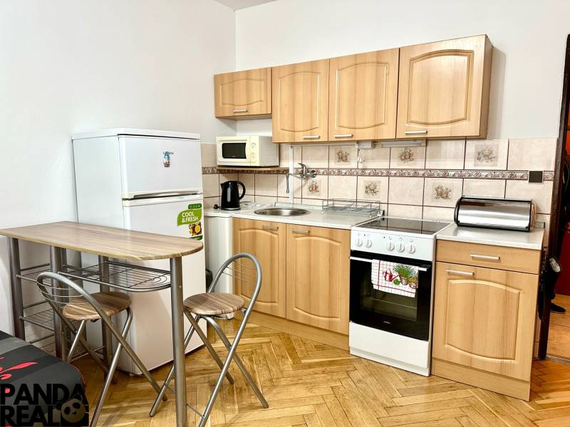 GARSONKA NA PRENÁJOM – VOĽNÁ IHNEĎ (sídlisko Východ) - Kuchyňa v garsónke s podlahou s dreveným dekorom, so spotrebičmi a sedením.