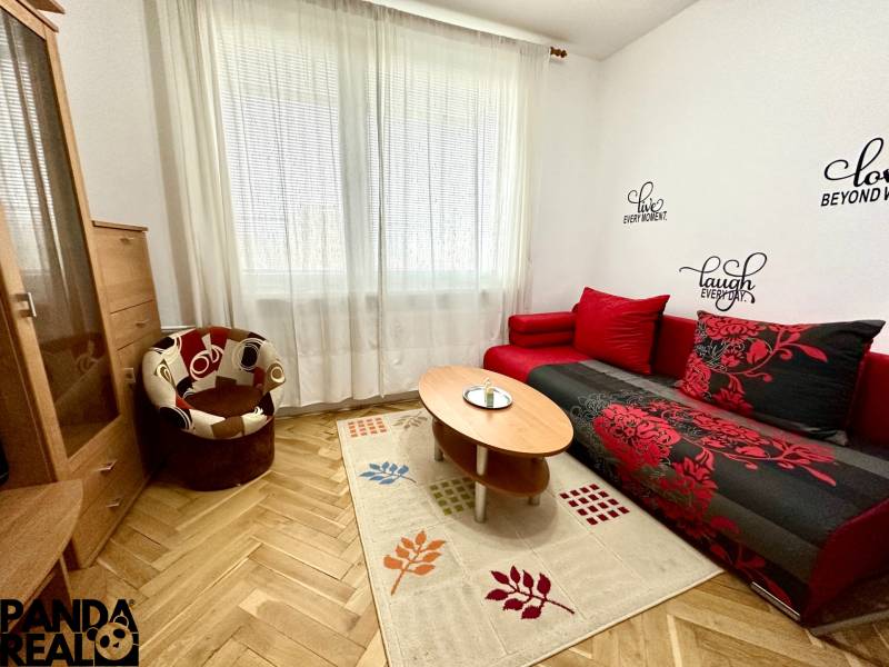 GARSONKA NA PRENÁJOM – VOĽNÁ IHNEĎ (sídlisko Východ) - Garsónka s podlahou s dreveným dekorom, červenou sedačkou a kreslom.