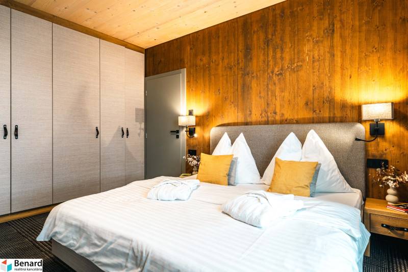 Na predaj krásny apartmám v Štrbe - Spálňa v 2-izbovom byte s posteľou, skriňou a stenou s dreveným dekorom.