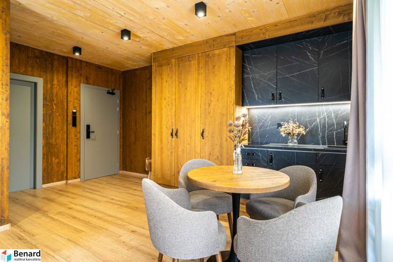 Na predaj krásny apartmám v Štrbe - Interiér 2-izbového bytu s podlahou s dreveným dekorom, drevenými stenami a čiernou kuchynskou linkou.