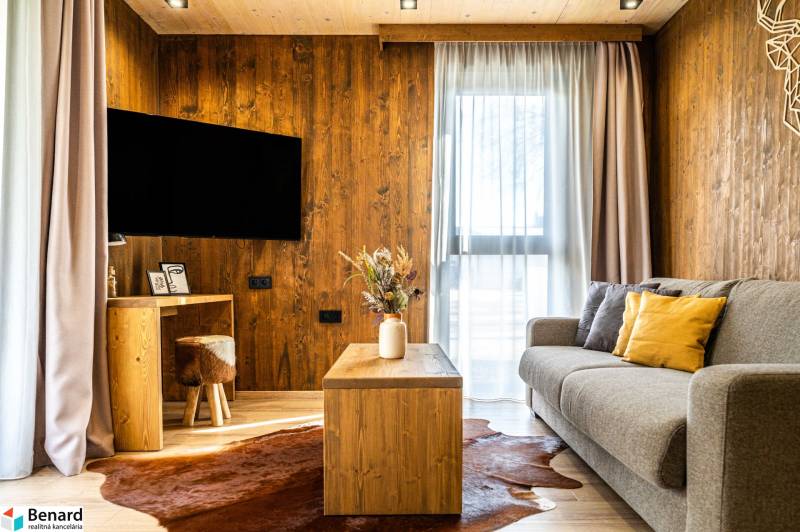 Na predaj krásny apartmám v Štrbe - Obývacia izba v 2-izbovom byte s pohovkou, podlahou s dreveným dekorom a konferenčným stolíkom.