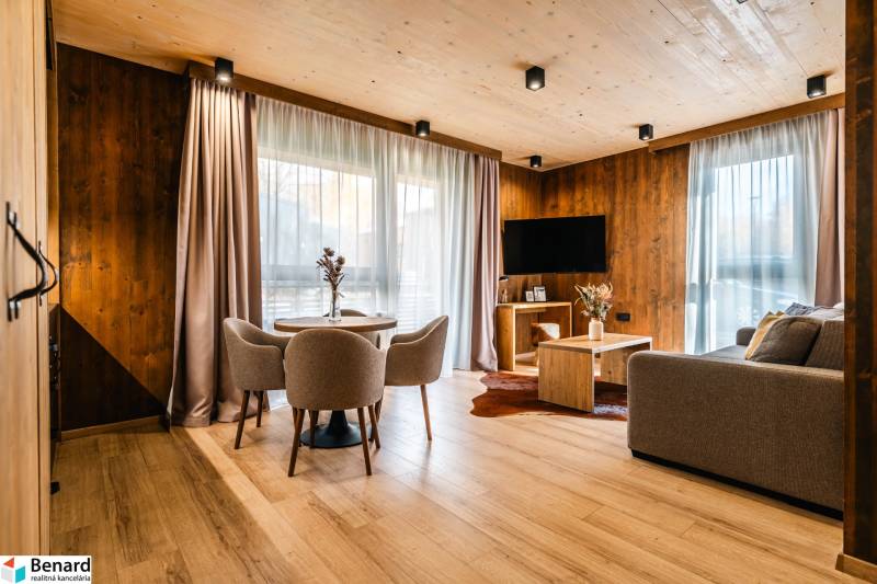 Na predaj krásny apartmám v Štrbe - Obývačka v 2-izbovom byte s podlahou s dreveným dekorom, sedačkou a jedálenským stolom.