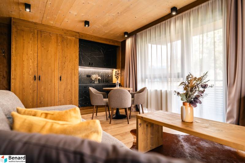 Na predaj krásny apartmám v Štrbe - Interiér 2-izbového bytu s podlahou s dreveným dekorom, štýlovým nábytkom a závesmi.