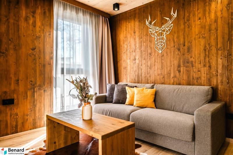 Na predaj krásny apartmám v Štrbe - Obývacia izba v 2-izbovom byte s podlahou s dreveným dekorom a dekoráciou na stene.