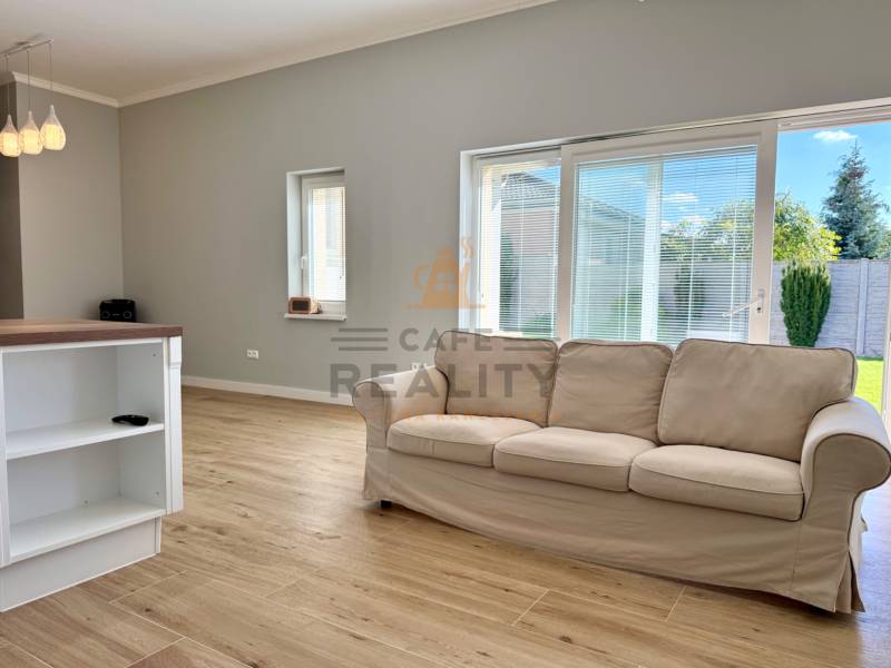 REZERVOVANÉ Na prenájom 4 izbový rodinný dom, Pata, ul. Pod Vinohradmi - Svetlá obývacia izba s podlahou s dreveným dekorom, pohovkou a výhľadom do záhrady.